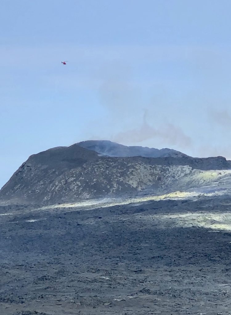 A red helicopter flying over the smoking crater of the erupting volcano in Iceland