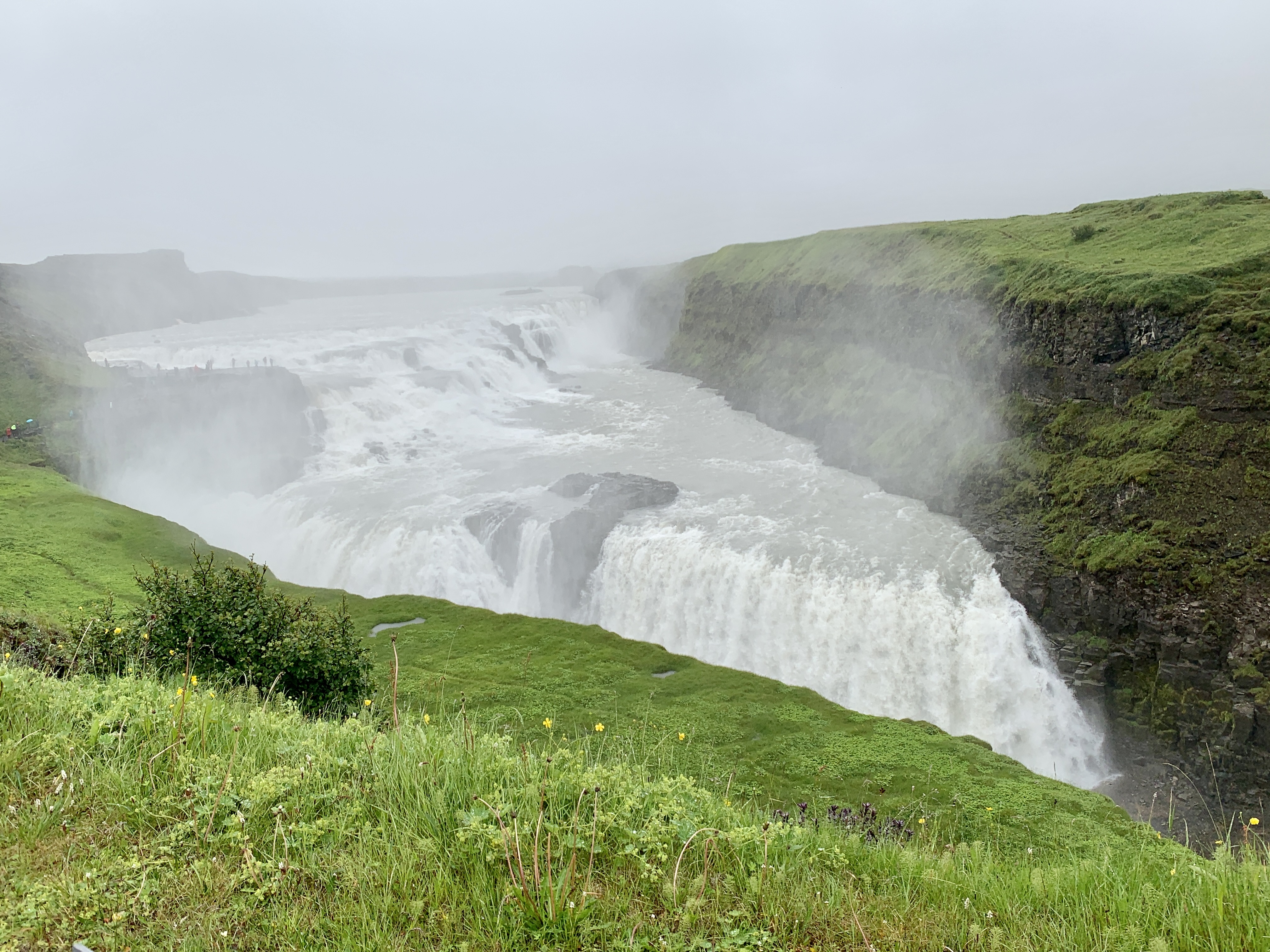 Glimpse of two levels of the Gullfoss Waterfall, surrounded by green cliffs